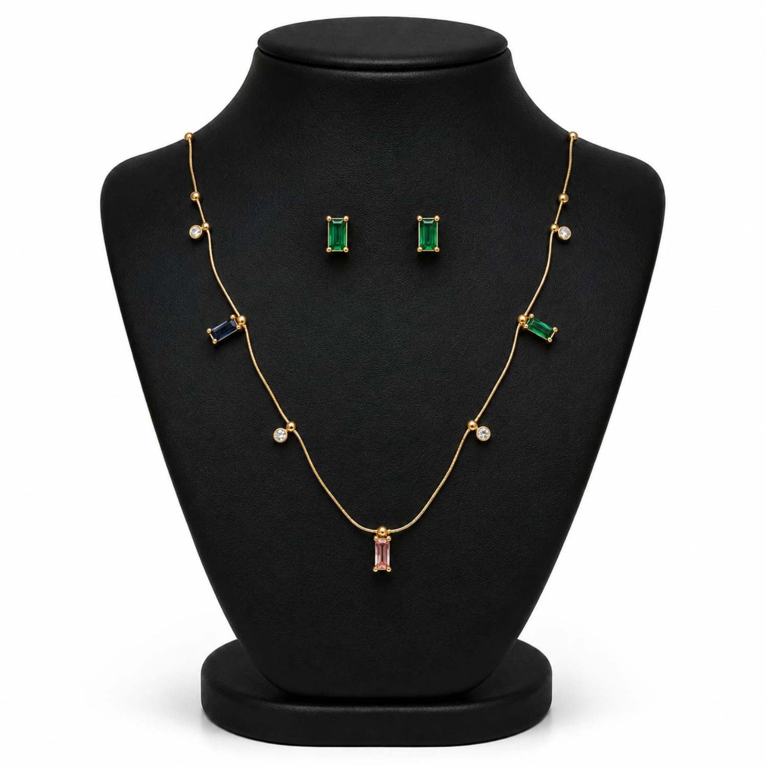 Gold jewelry set displayed on a black mannequin bust, including a necklace with green, blue, and pink baguette stones, matching rectangular stud earrings, and small round pearl-like accents.
