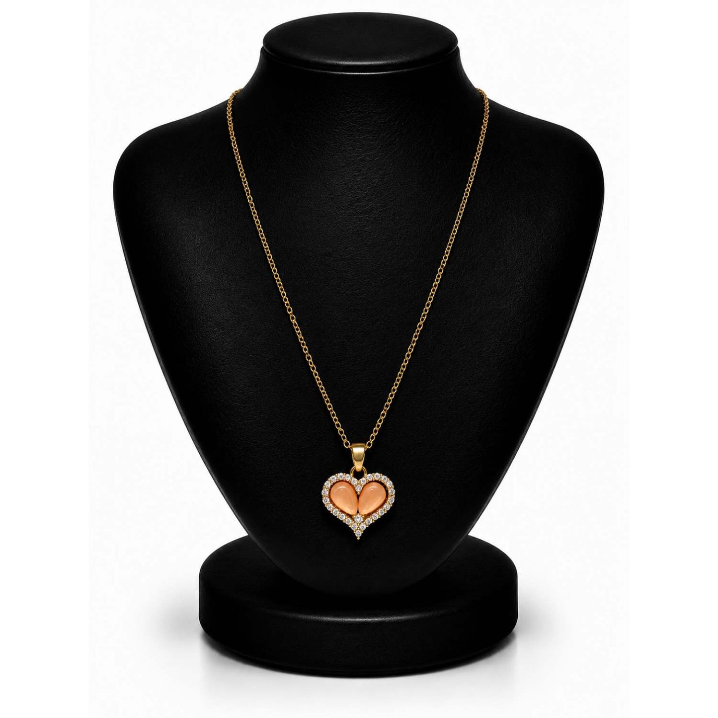 A gold heart pendant necklace with a peach-colored center, displayed on a black jewelry bust against a white background.