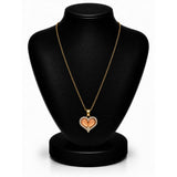 A gold heart pendant necklace with a peach-colored center, displayed on a black jewelry bust against a white background.
