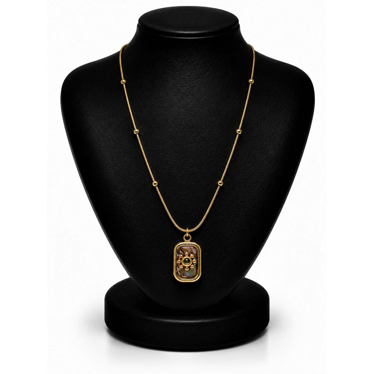 A gold necklace with a rectangular pendant featuring a floral design, displayed on a black jewelry bust against a white background.