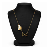 A gold chain necklace displayed on a black jewelry bust, featuring a butterfly pendant with white enamel detailing and a small bow charm at the bottom.