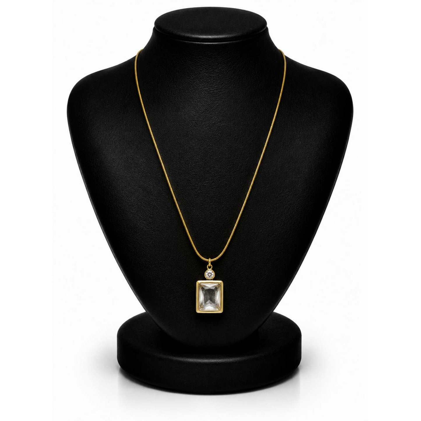 A gold chain necklace with a square bezel-set clear gemstone pendant, displayed on a black jewelry bust against a white background.
